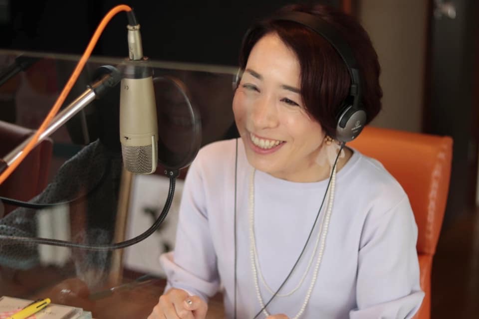 ラジオスタジオのマイクの前で笑顔を見せる土居由紀子